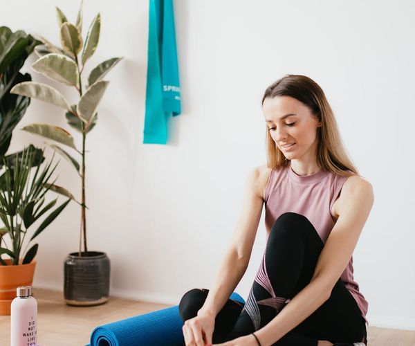A simple yoga mat rolled out on a wooden floor next to a water bottle.